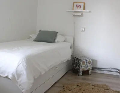 a small bedroom with a white bed and a nightstand at Strandlicht in Egmond aan Zee