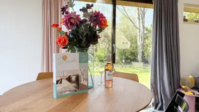 a table with a bottle of whiskey and a vase of flowers at Het Duinhuisje by Droomvilla in Egmond aan den Hoef