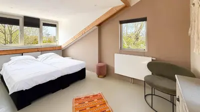 a bedroom with a bed and a chair and windows at Het Duinhuisje by Droomvilla in Egmond aan den Hoef
