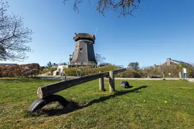a bench in a field with a lighthouse in the background at Villa Koperwiek in Egmond aan den Hoef