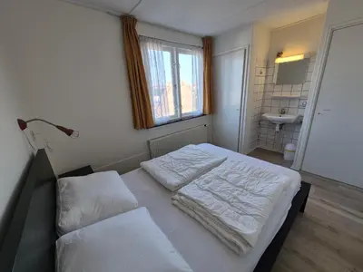 a bedroom with a bed with white sheets and a sink at De Groten Zes in Egmond aan Zee