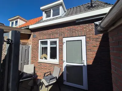 a brick house with a door and two chairs at Vlier aan zee in Katwijk aan Zee