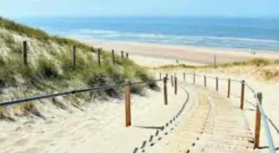 a wooden path on a sandy beach near the ocean at Huisje Suus, inclusief jacuzzi, kano en kajak in Zuid-Scharwoude