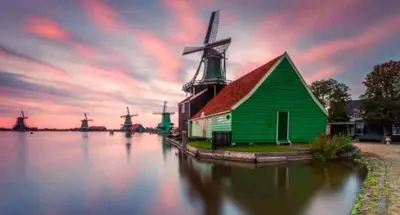 a green barn with a windmill in the water at Huisje Suus, inclusief jacuzzi, kano en kajak in Zuid-Scharwoude
