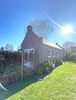 a brick house with a fence in a yard at Huisje Suus, inclusief jacuzzi, kano en kajak in Zuid-Scharwoude