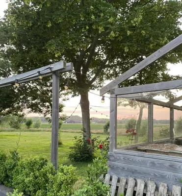 a wooden pergola next to a tree in a field at Tiny House Egmond in Egmond aan den Hoef