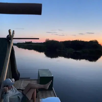 two people sitting on the dock of a boat on a lake at Campingraft Katwoude in Katwoude