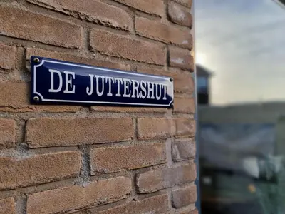 a blue sign on the side of a brick wall at De Juttershut in Egmond aan Zee