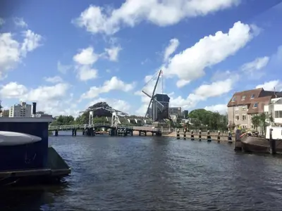 a river with a bridge and a windmill in the background at Lovely cozy houseboat Rembrandt, old centre Leiden in Leiden