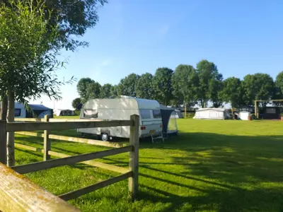 a rv parked in a field next to a fence at Trekkershut - De Hollandse Boerderij in Ons Belang