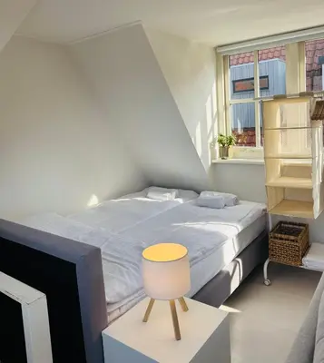 a small bedroom with a bed and a yellow chair at tiny beach house noordwijk in Noordwijk aan Zee