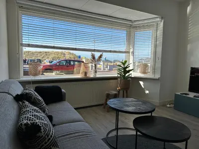 a living room with a couch and tables and a window at Zin aan Zee in Egmond aan Zee
