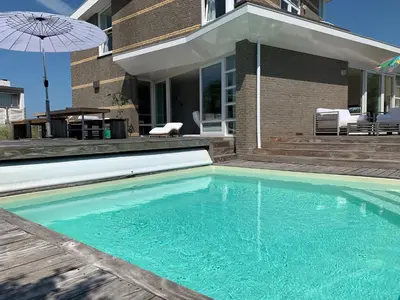 a swimming pool in front of a house with an umbrella at Heerlijke villa met zwembad en sauna bij het strand in Bergen aan Zee