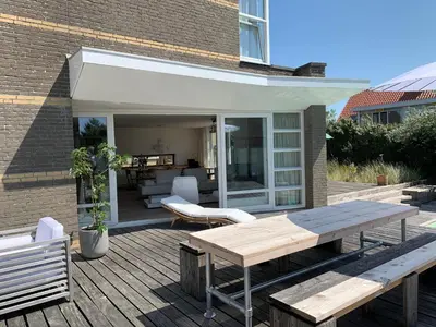 a wooden deck with a table and a bench at Heerlijke villa met zwembad en sauna bij het strand in Bergen aan Zee