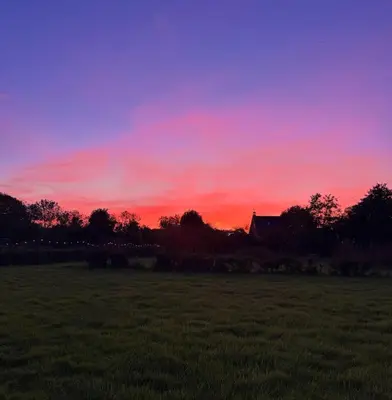a sunset in a field with a house in the background at Bed and Breakfast Het schapenlandje in Waarland