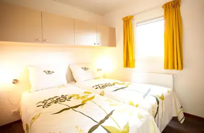 a bedroom with two beds with yellow curtains and a window at EuroParcs Buitenhuizen in Velsen-Zuid