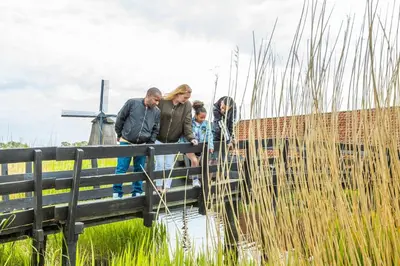 a group of people standing on a bridge with a windmill at EuroParcs Molengroet in Noord-Scharwoude