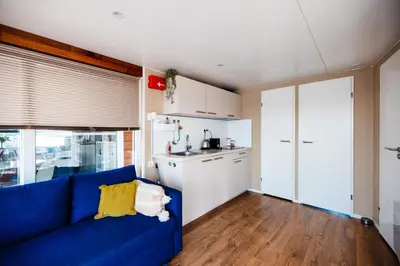 a living room with a blue couch and a kitchen at Floating Holiday Home - 15 mins to AMS in Vinkeveen