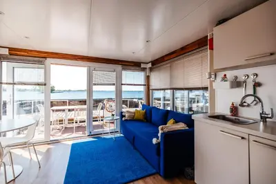 a living room with a blue couch and a kitchen at Floating Holiday Home - 15 mins to AMS in Vinkeveen