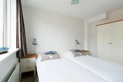 a white bedroom with two beds and a window at Boathouse Suburban Amsterdam in Uitgeest