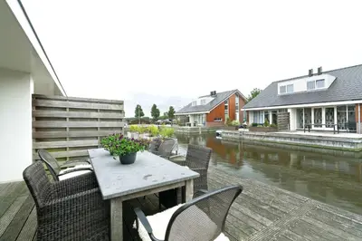 a patio with a table and chairs next to a river at Boathouse Suburban Amsterdam in Uitgeest