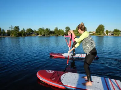 two women are standing on paddle boards in the water at Unique Tiny House close to Ams Airport with Hottub in Rijsenhout
