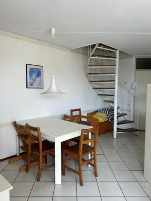 a dining room with a table and chairs and a spiral staircase at Gemütliches Ferienhaus am Meer in Ons Belang
