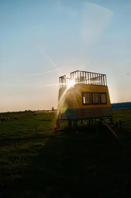 a tiny house in a field with the sun setting at Hihahut De Zonnepost in Oud-Ade
