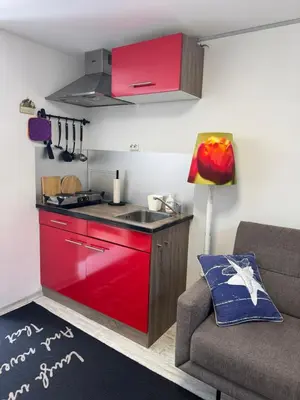a small kitchen with a red cabinet and a couch at Zomerhuisje Maranatha in Noordwijk aan Zee
