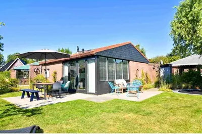 a house with a patio with chairs and an umbrella at The Kingfisher near beach and dunes Hargen and Schoorl in Dirkshorn