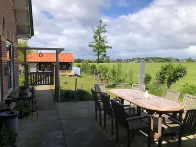a patio with a wooden table and chairs and a field at kleinrosenbrand in Burgerbrug
