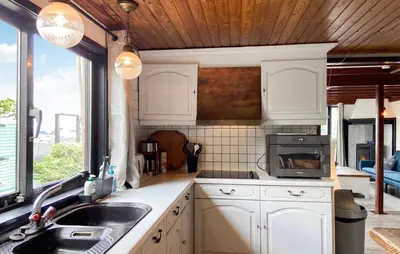 a kitchen with white cabinets and a sink and a window at Woonboot De Karekiet in Loosdrecht
