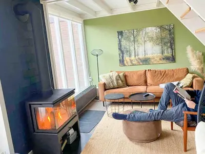 a woman sitting in a living room with a fireplace at The Highlander- Stylish Hideaway near Beach & Forest Schoorl and Bergen- Dogs Welcome in Warmenhuizen