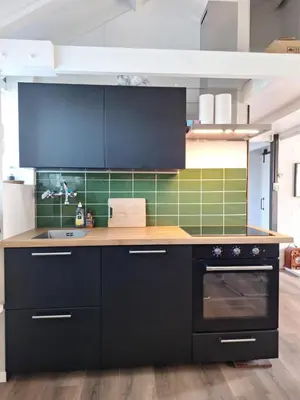 a kitchen with black cabinets and green tiles at Rekerlanden 32 in Schoorldam