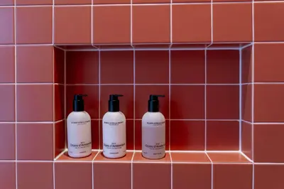 three shampoo bottles in a red tiled bathroom wall at Suite Palette in Amsterdam