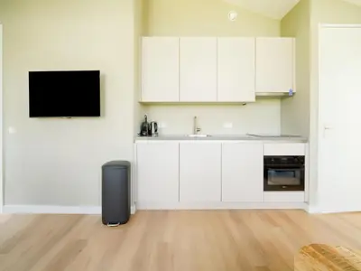 a kitchen with white cabinets and a tv on the wall at Holiday Home Oud Ade near Kaag Lakes in Oud-Ade