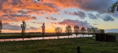 a sunset over a river with trees and a bridge at B&B Krachtwijk in Soest