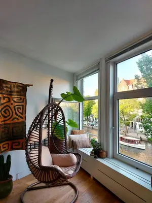 a room with a rattan chair in front of a window at Canal House with a Unique View in Amsterdam