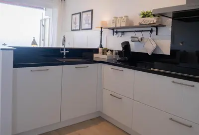 a kitchen with white cabinets and a black counter top at Seaviews Egmond in Egmond aan Zee