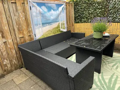 a black wicker bench with a table on a patio at Zon Zee en Duin Egmond Strandhuisje in Egmond aan Zee