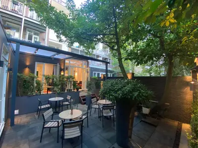 a patio with tables and chairs and a tree at Alp Hotel in Amsterdam