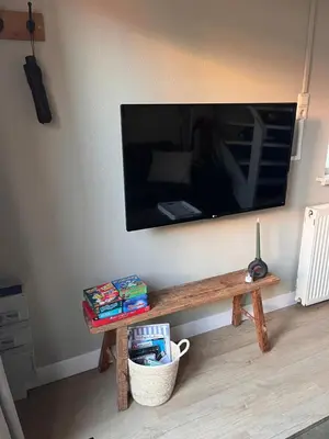 a living room with a table with a tv on the wall at Beachhouse Noteboom, omheinde tuin in Noordwijk aan Zee