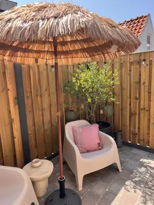 a chair under a straw umbrella on a patio at Beachhouse Noteboom, omheinde tuin in Noordwijk aan Zee
