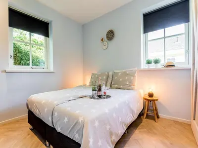 a bedroom with a bed with white sheets and two windows at Bungalow near Dutch Coast & Forest in Noordwijk
