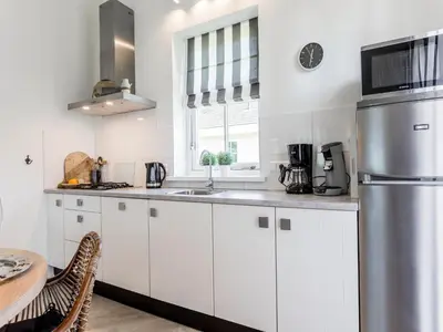 a kitchen with white cabinets and a sink and a table at Bungalow near Dutch Coast & Forest in Noordwijk