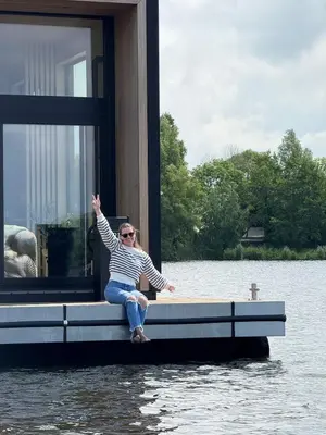 a woman sitting on a dock in the water at Modern Stay Tiny Houseboat to visit Amsterdam in Monnickendam