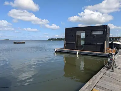 a black house on a dock on a body of water at Modern Stay Tiny Houseboat to visit Amsterdam in Monnickendam