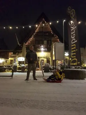 a man standing next to a child on a sled in the snow at Duinberk B&B hotel en Brasserie in Schoorl