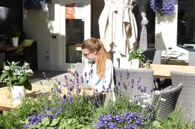 a woman sitting at a table with purple flowers at Duinberk B&B hotel en Brasserie in Schoorl