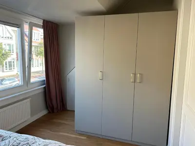 a bedroom with white cabinets and a window at Appartement Huis ter Duinstraat in Noordwijk aan Zee